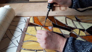Soudure d'un vitrail pendant le stage et les cours de vitrailliste dans un atelier dans le Perche